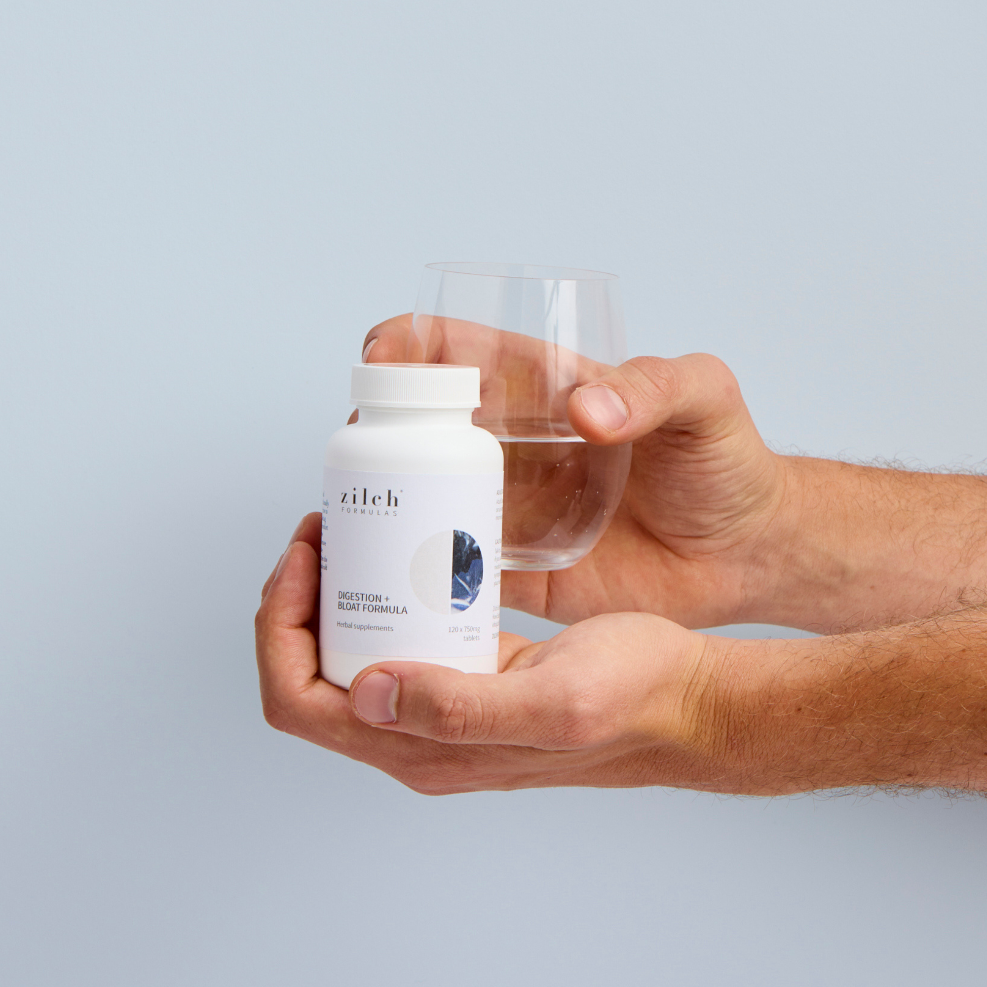 Zilch digestion and bloat formula held by male hand with glass of water